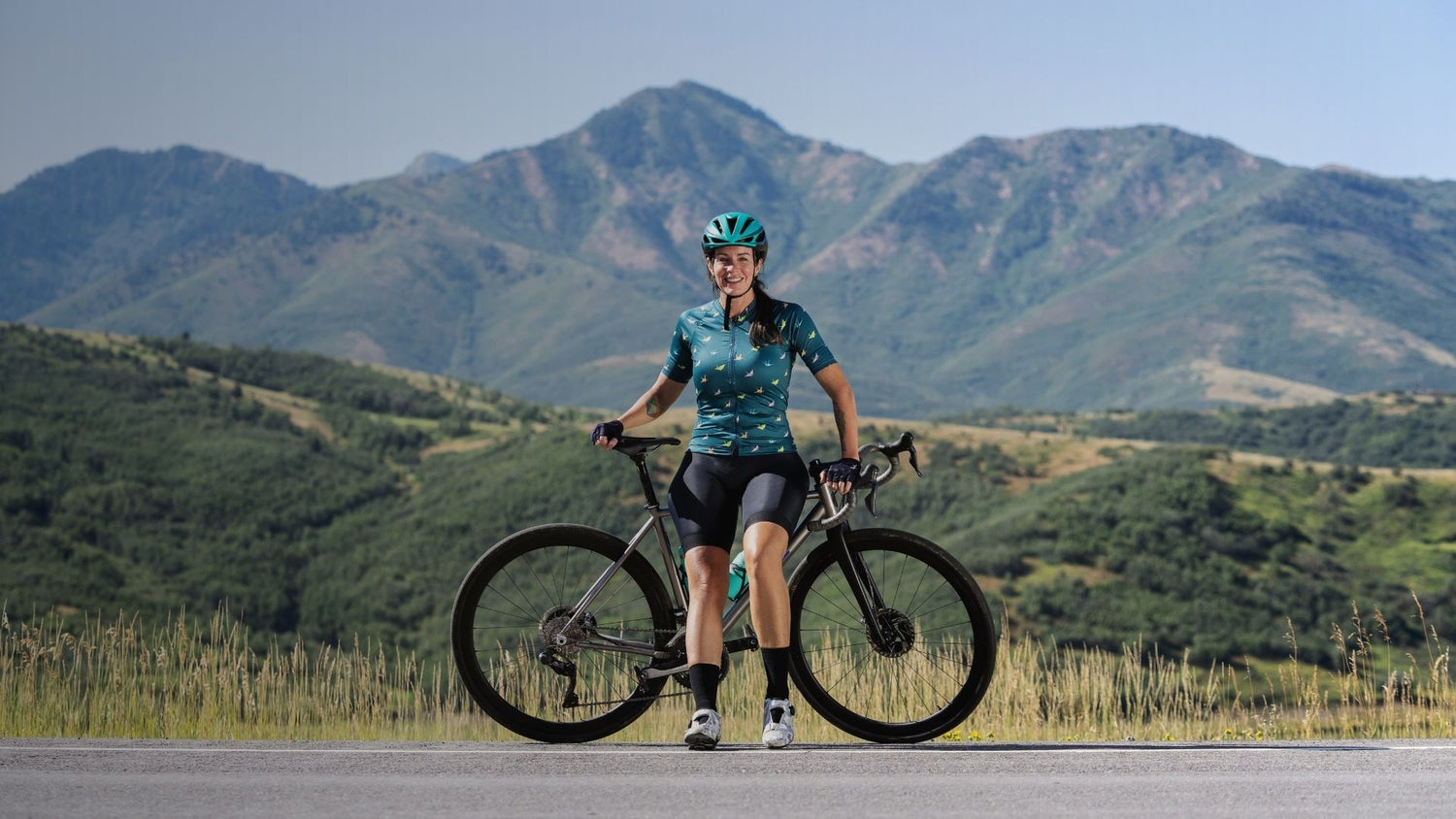 Person with a bicycle on a road with mountains in the background
